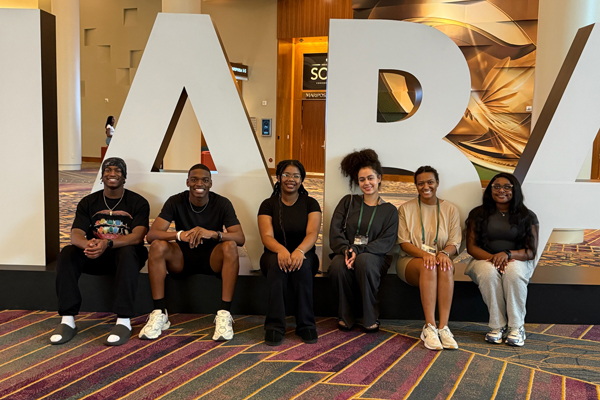 NABA members sit in front of large white letters reading NABA during a national conference.
