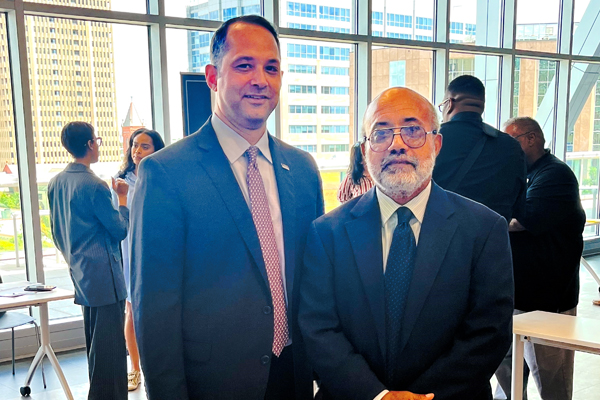 Two men in suits and ties smile for a photo. 