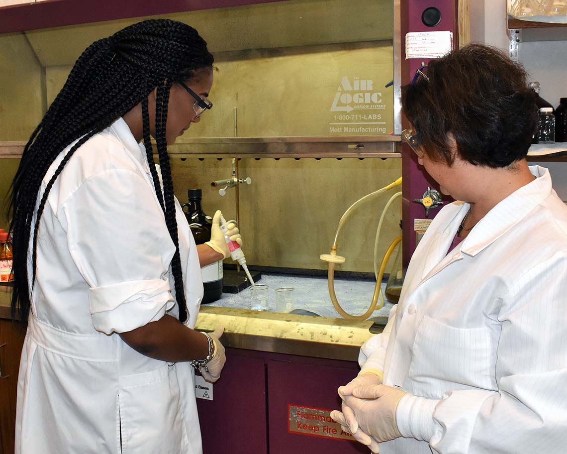 Two scientists stand pippette in front of a fume hood