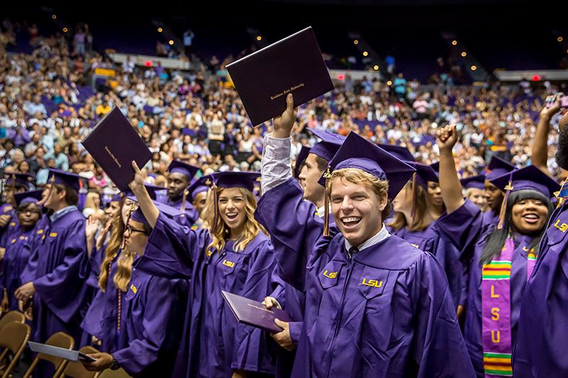 LSU students celebrating graduation dressed in regalia holding their diplomas high in the air.