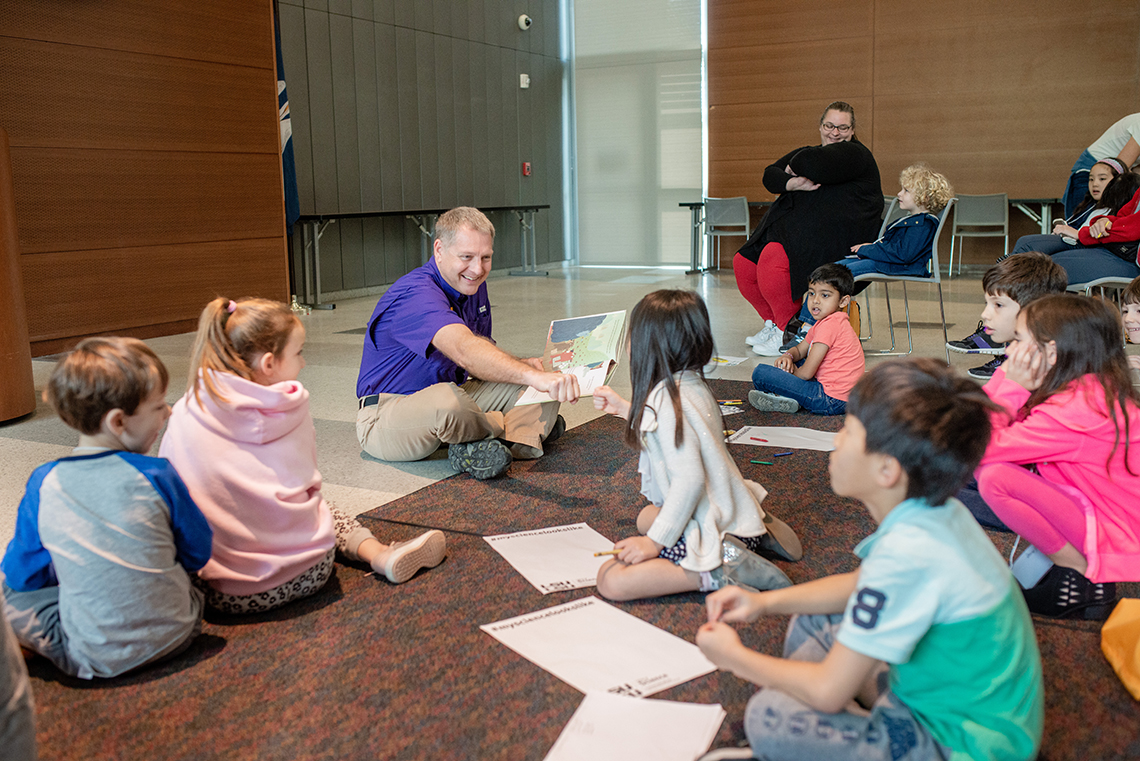 Dr. Kyle Harms fist bumps a STEM Story Time participant while reading them a book.